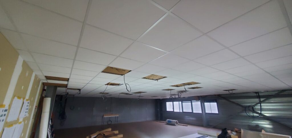 Détail de la pose d'une ossature métallique pour plafond modulaire démontable, garantissant un alignement parfait des dalles